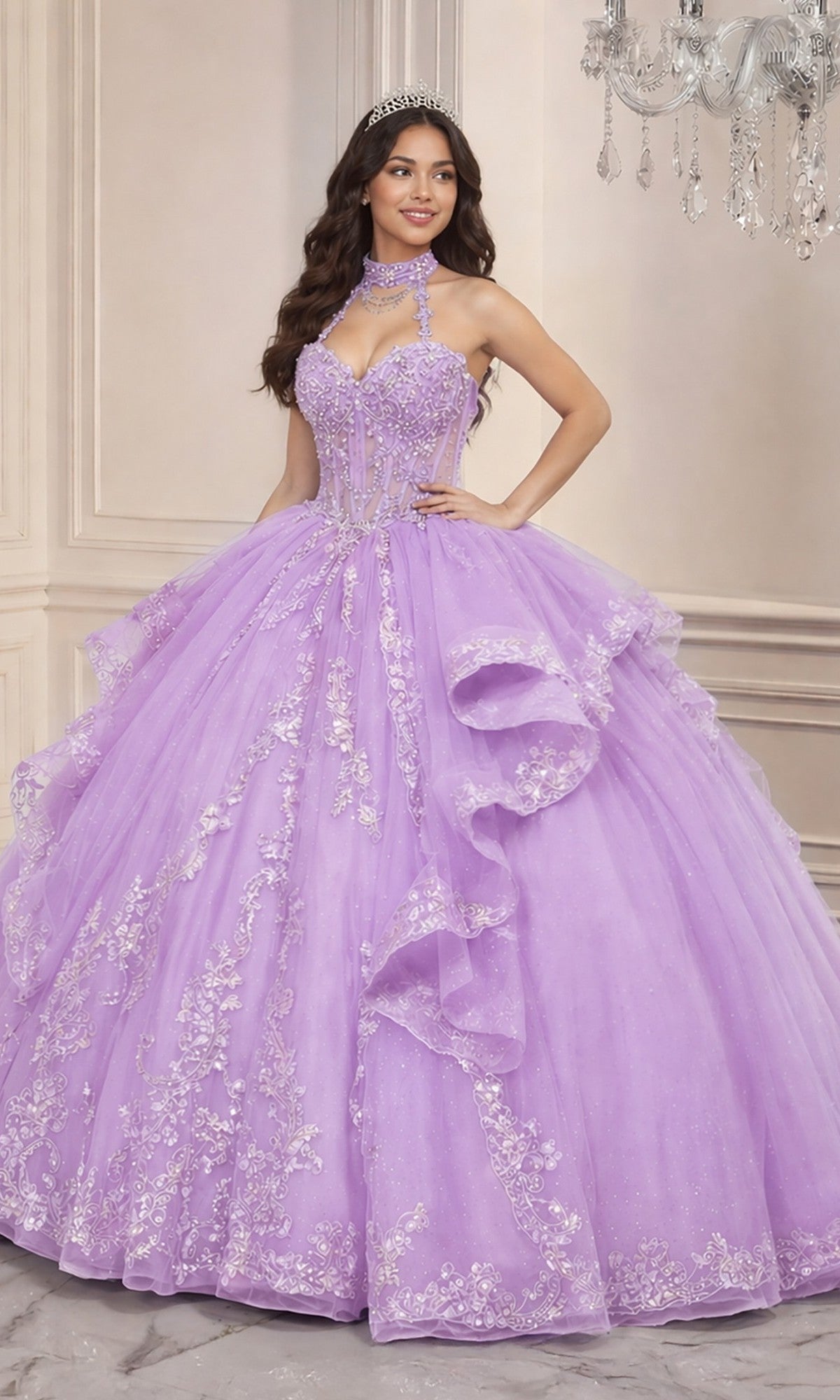 A woman wears the Quinceanera Dress 15741 By Ladivine in lilac, adorned with silver embroidery and a tiara, standing indoors by a chandelier. Layers of glitter tulle enhance her magical and elegant quinceanera style.
